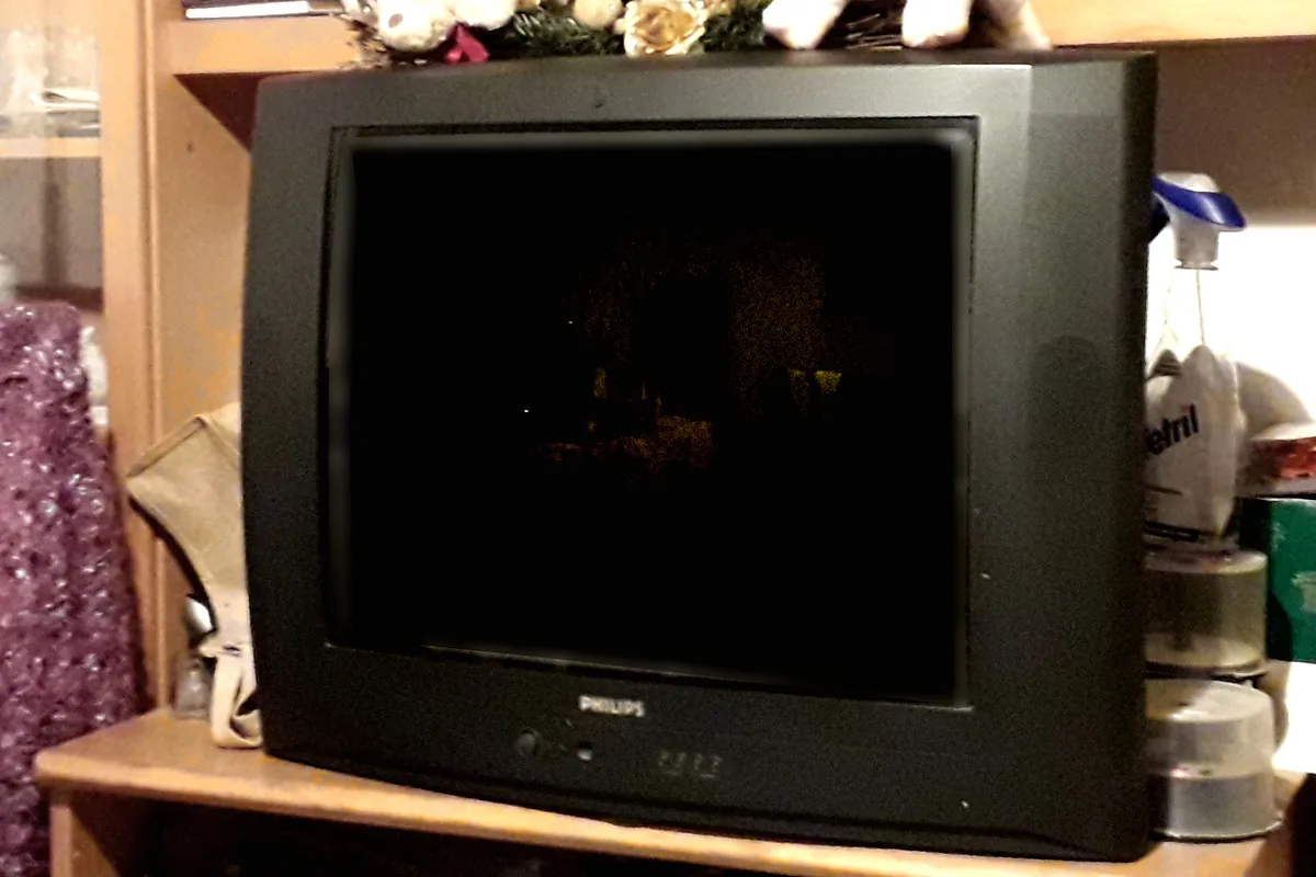 Televisor de tubo Philips preto sobre um móvel de madeira, tela desligada, típico da era das TVs de tubo