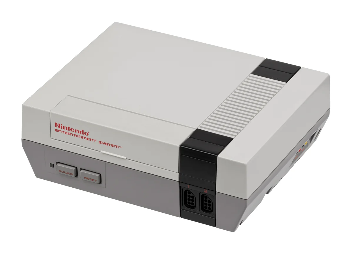 Foto de um Nintendo Entertainment System modelo NES-001, carcaça cinza com painel preto, dois botões vermelhos e LED laranja
